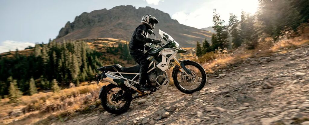 A rider navigating a dirt trail on a motorcycle with a mountainous background, showcasing off-road riding skills in a natural environment.