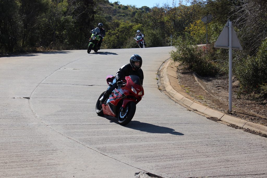 Three riders lean into a bend on a concrete training circuit during a cornering course