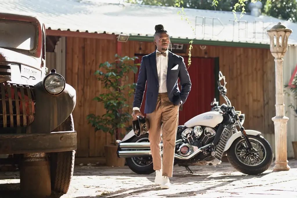 Dapper rider in a blazer and bow tie beside a cream cruiser at the Distinguished Gentleman's Ride