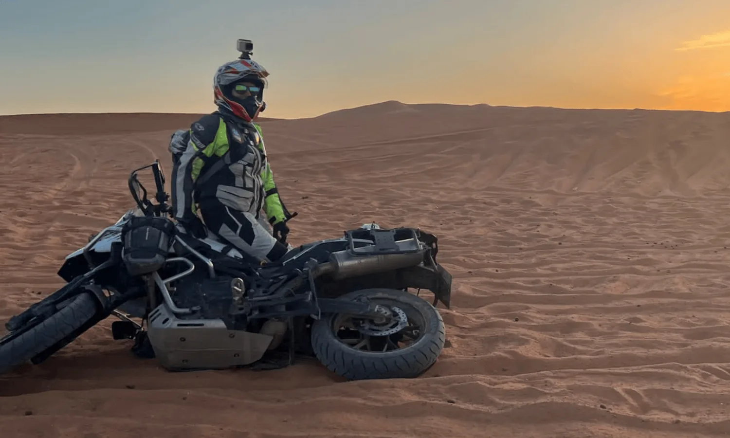Rider beside a fallen adventure bike in the desert at sunset