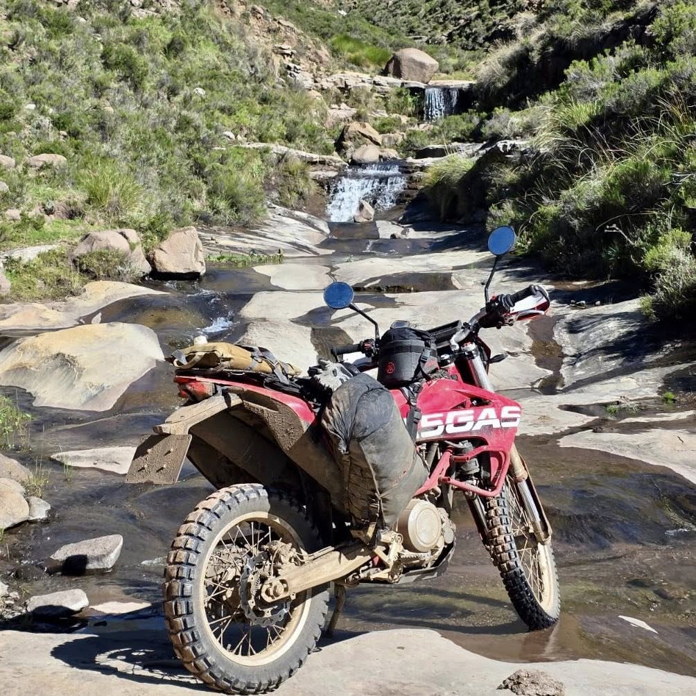 GasGas dual-sport bike parked on rocks beside a mountain stream