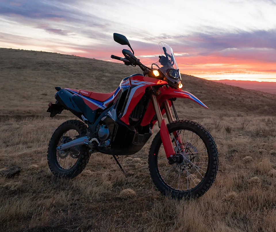 Red Honda CRF300 Rally parked on grassland at sunset