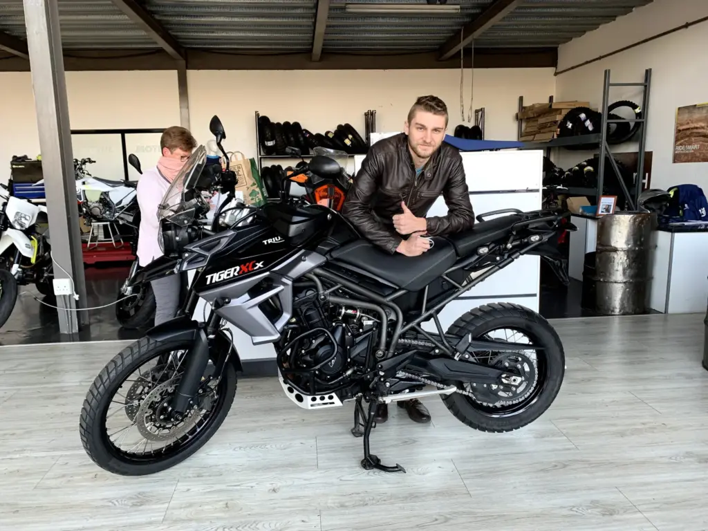 Rider giving a thumbs up beside a Triumph Tiger 800 XCx in a showroom