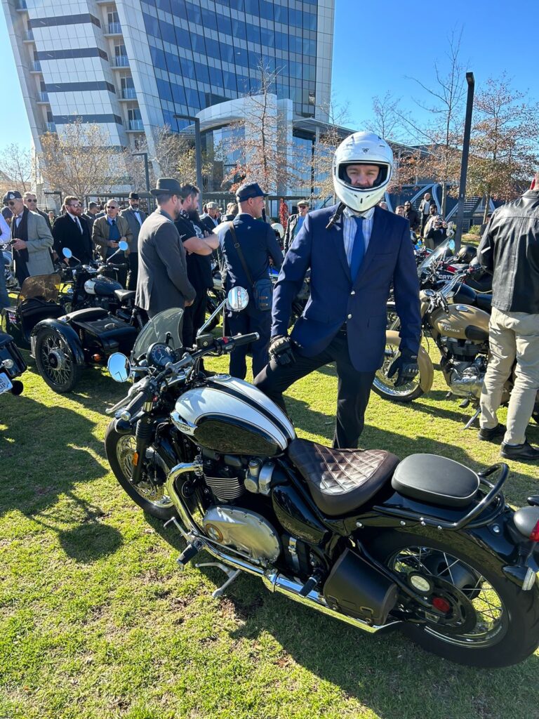 Rider in a suit and white helmet with his motorcycle at the Distinguished Gentleman's Ride