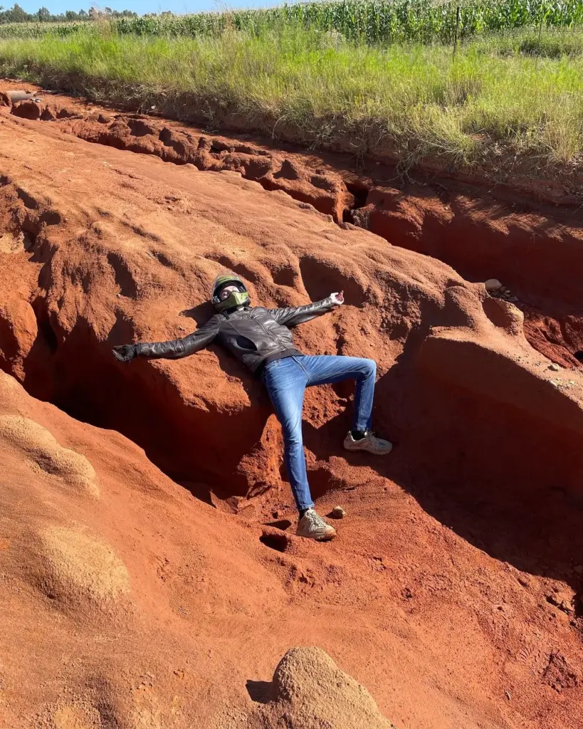 Rider lying with arms outstretched in a red dirt erosion gully