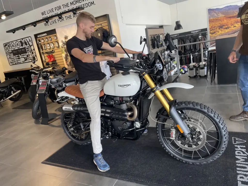 Rider sitting on a white Triumph Scrambler 1200 in a Triumph showroom