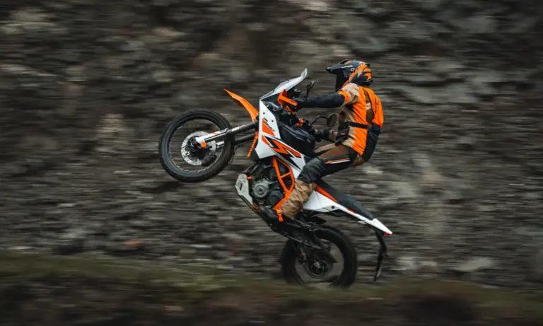 Rider wheelieing a KTM 390 Adventure R past a rock wall