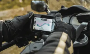 Gloved hand beside a handlebar-mounted GPS showing a route