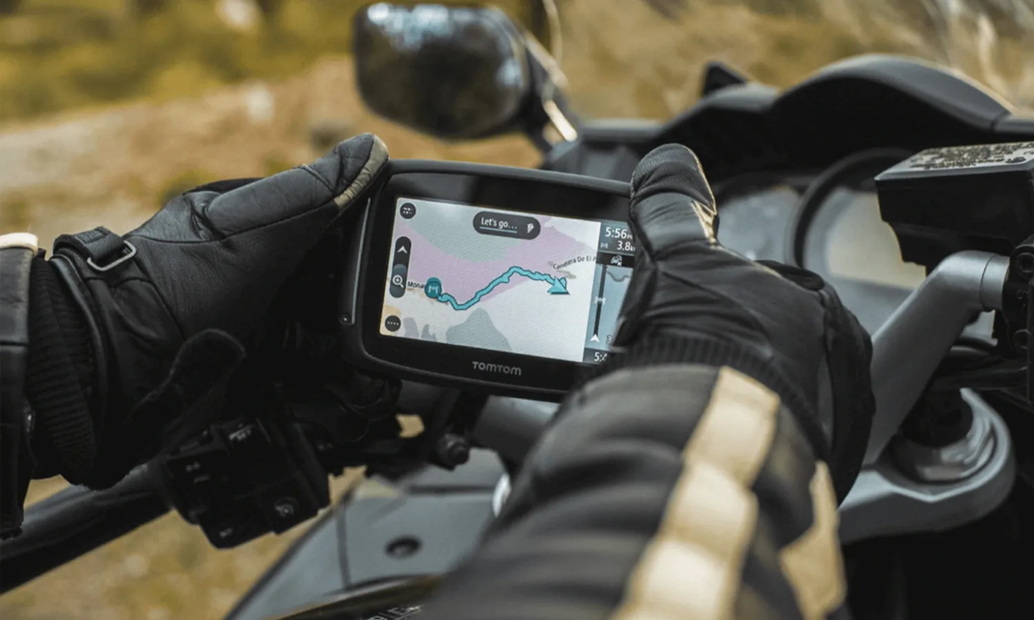 Gloved hand beside a handlebar-mounted GPS showing a route