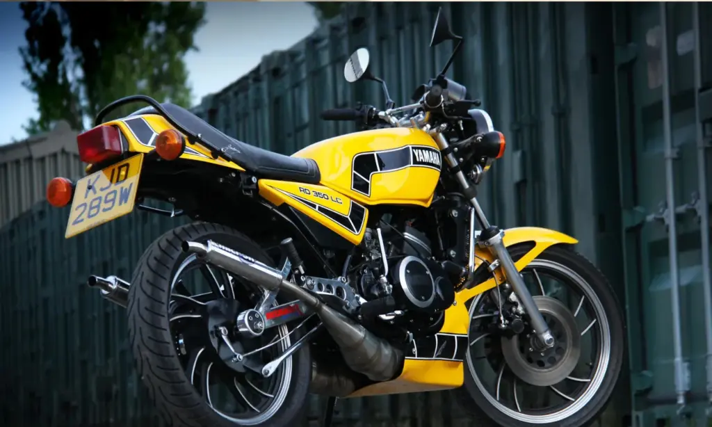 Yellow and black Yamaha RD350LC parked beside a shipping container