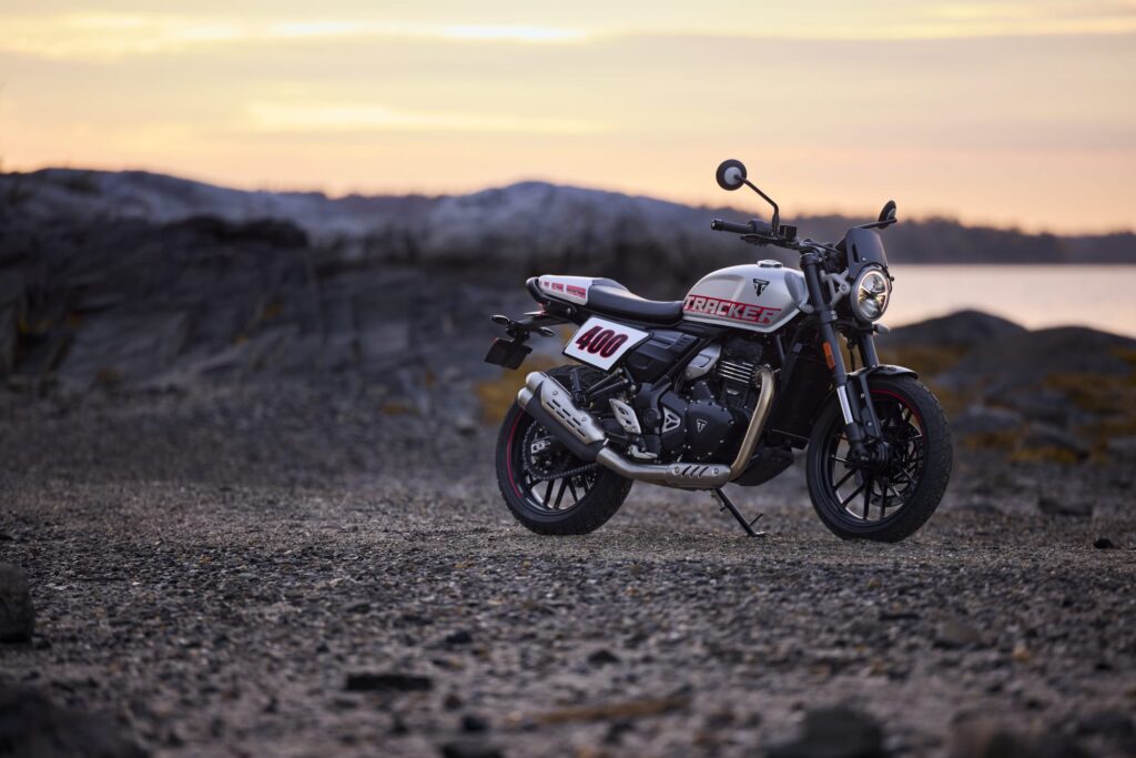 Triumph Tracker 400 in Aluminium Silver with red race graphics, parked on gravel at dusk
