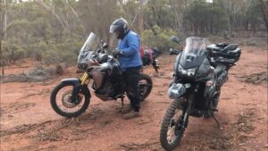 Two loaded adventure bikes stopped on a red dirt track in the bush