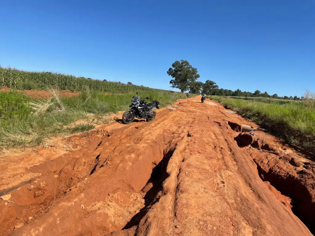 Two Triumph Tiger 800 XCx motorcycles on a deeply rutted red dirt road